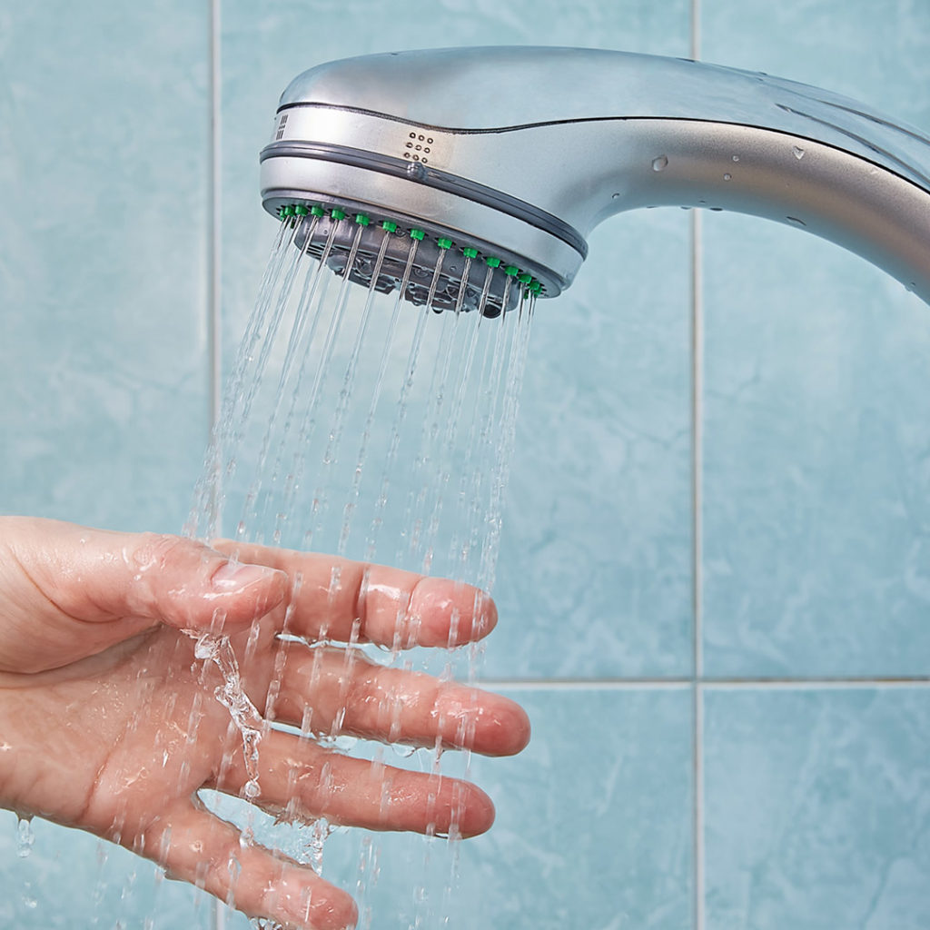 Person sticking their hand in the water stream from a showerhead. 